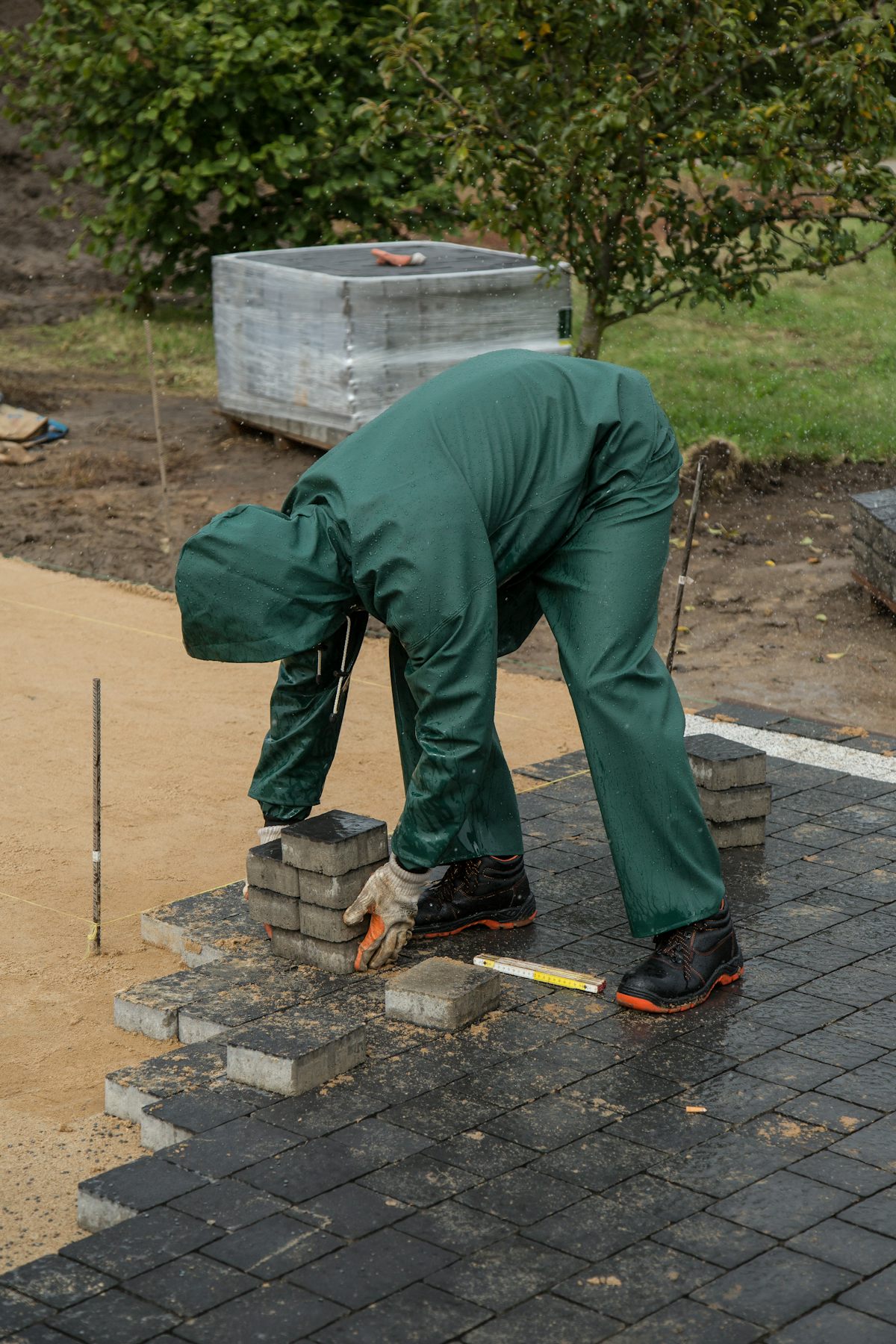 Vakman in werkkledij legt donkere betonklinkers op een vlak zandbed