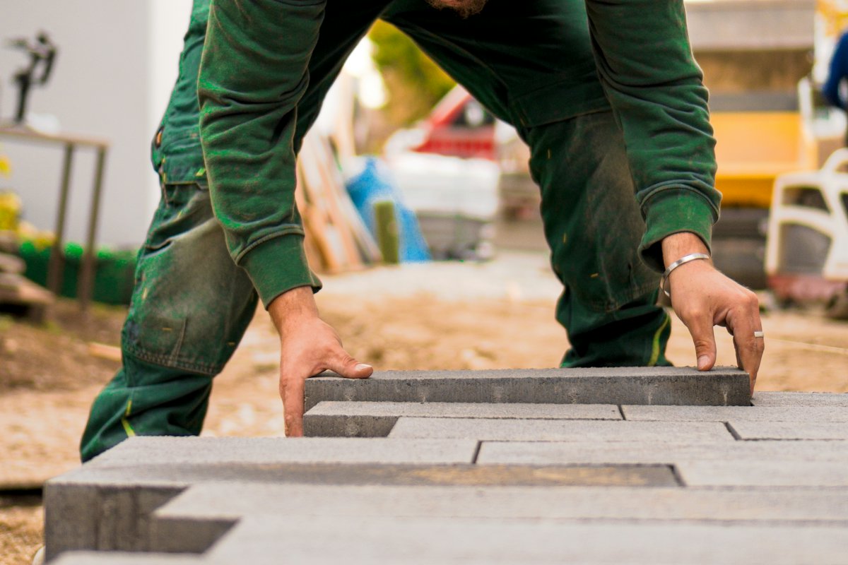 Handen die een grijze betonklinker op zijn plaats leggen, naast een rij die al ligt